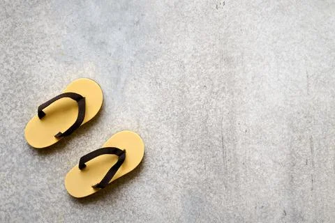 Tiny decorative flip-flops on gray concrete background close-up with space fo Stock Photos