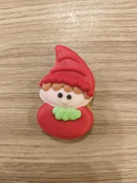 Tiny elf with red hat and green scarf sits on wooden surface Stockfoto's