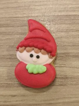 Tiny elf with red hat and green scarf sits on wooden surface Stockfoto's