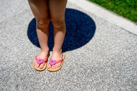 Tiny feet in pink flip-flops stand on stone Stock Photos
