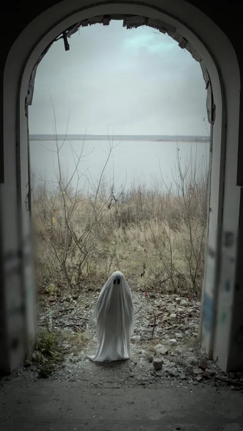Tiny figure in classic ghost sheet framed by ruined arch, overcast sky, river Stock Footage 320248488