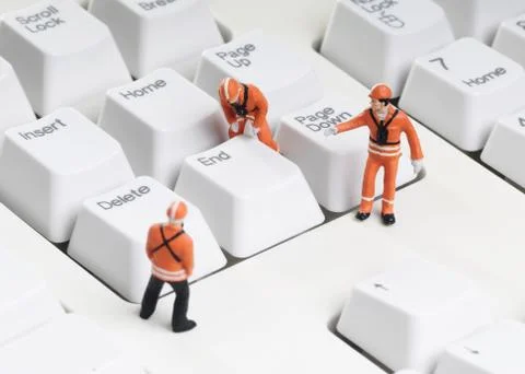 Tiny figures of construction engineers removing end key from computer keypad Stock Photos