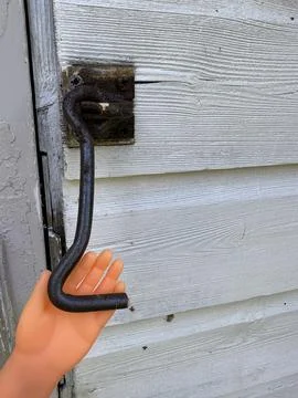Tiny finger puppet hand holding cabin hook attached to a wooden shed wall Stock Photos