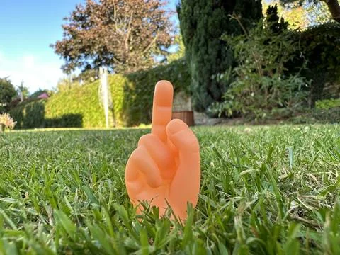 Tiny finger puppet hand showing middle finger, garden on the background Stock Photos