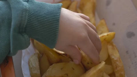 Tiny fingers grasp a single fry from a plate in close-up. The shot shows texture Stock Footage 315757546