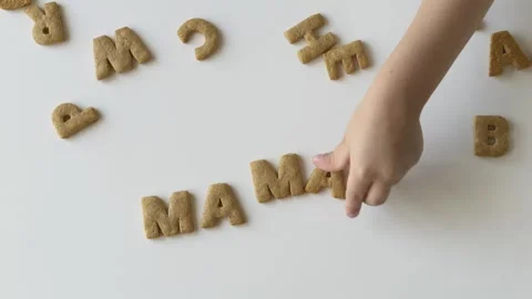Tiny fingers move letter cookies across a bright table, makes the word mama out Stock Footage 318293492