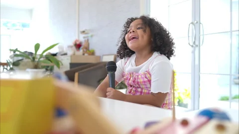 A tiny girl sits on a toy table, clutching a microphone Stock Footage 292617805