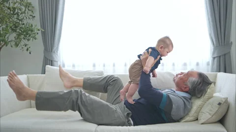 A tiny grandchild smiling happily on the couch with grandfather Stock Footage 287996828