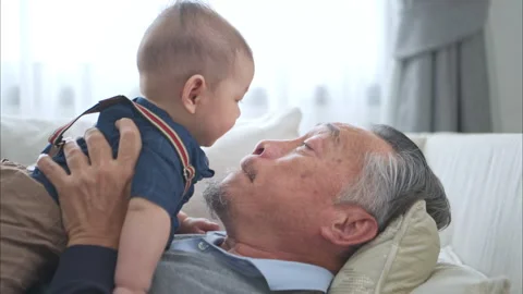 A tiny grandchild smiling happily on the couch with grandfather Stock Footage 287997024