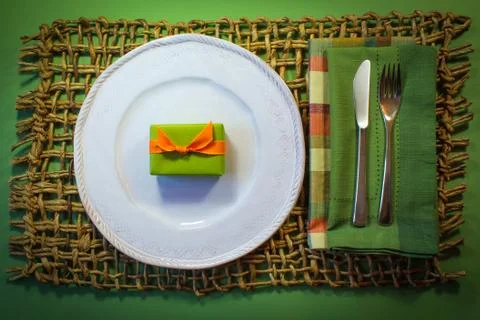 Tiny green gift box with orange ribbon on a white plate Stock Photos