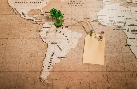 Tiny human models on price tag on world map with palm tree Stock-Fotos