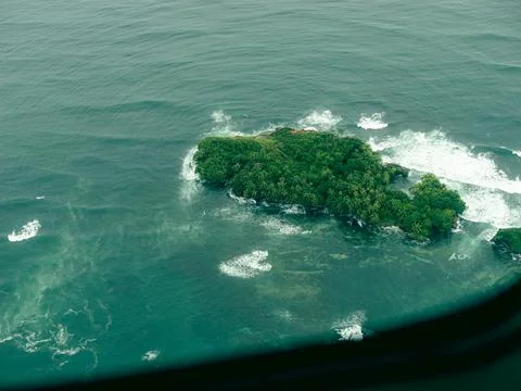 Tiny island covered in dense greenery floats in turquoise ocean waters Stock Photos