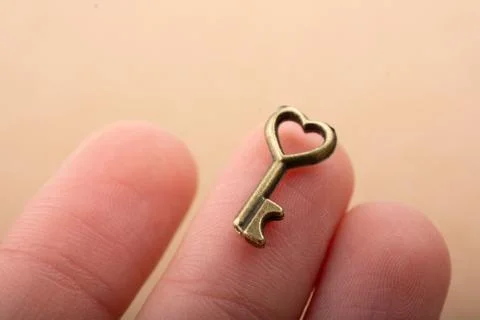 Tiny key with heart shape on the finger tip 스톡 사진