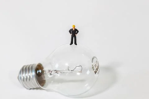 Tiny man standing on a light bulb on white background Stock Photos