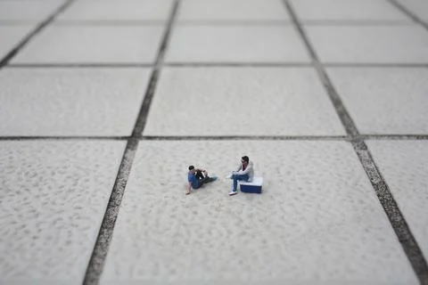Tiny model people rest casually across wide textured tiles Foto stock