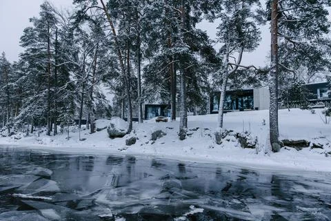 Tiny modern houses situated among snow-covered pine trees along the banks of an Stock Photos