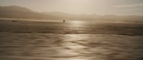 Tiny motorcycle in distance closes toward moving camera on dry lake Stock Footage 136495786