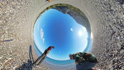 A tiny planet effect capturing a couple throwing stones into the sea, with a Stock Footage 294433094