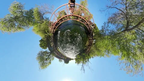 A Tiny Planet effect shows a circular view of a river flowing under a wooden 스톡 동영상 289794723