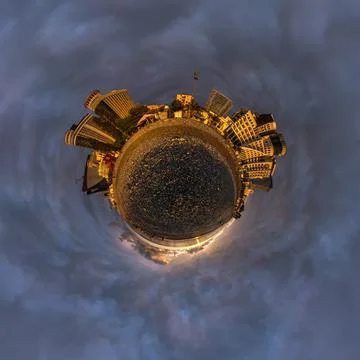 Tiny planet in evening sky in city center near modern skyscrapers near sea co Stock Photos