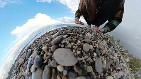 Tiny Planet perspective showing a woman collecting stones on a pebble beach, Stock Footage 293277546