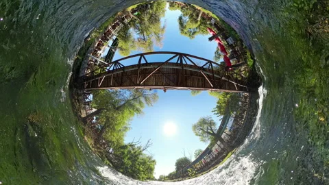 A Tiny Planet view of a wooden bridge over a river, surrounded by lush green Video stock 289794136