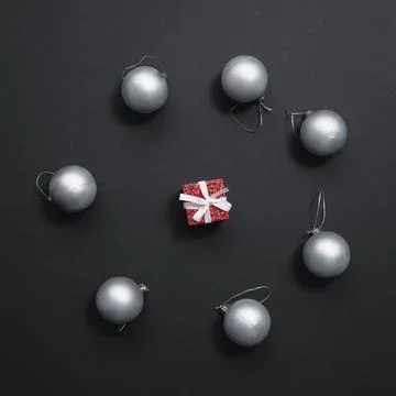 A tiny red gift box lies in the center of blue Christmas balls on a matte black Stock Photos