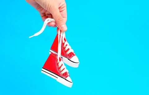 Tiny Red High-Top Canvas Shoes in Hand on Blue Background 스톡 사진