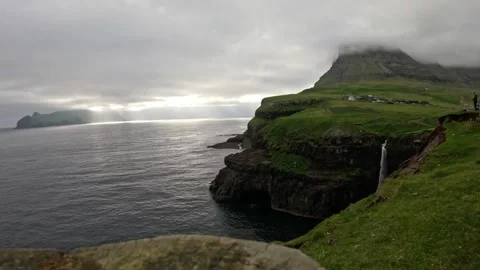 Tiny silhouette of a person looking at Múlafossur waterfall, Faroe Islands Vidéo 337558572