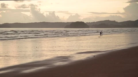 Tiny silhouette romantic couple walking together on beach in evening Stock Footage 153507477