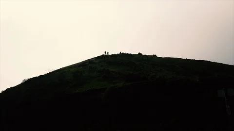 Tiny Silhouetted Figures climb and play atop a hill at evening. Stock Footage 89237640
