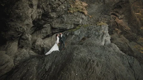 Tiny silhouettes of bride and groom kissing on rocks, Reynisfjara beach, Iceland Stock Footage 254395336