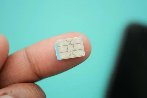 Tiny SIM card held between fingers against blue background Foto stock
