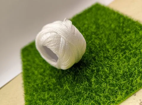 Tiny thread spool rests on a bed of vibrant green. Soft focus, warm light. .. Stock Photos