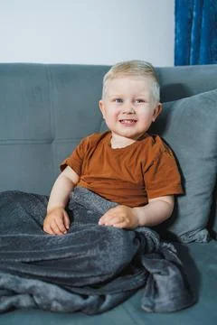 Tiny toddler sitting cheerfully on sofa with warm light. Young child enjoying Stock Photos