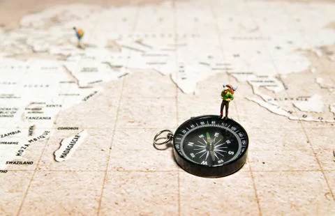 Tiny traveler model stand on compass over brown map Stock Photos