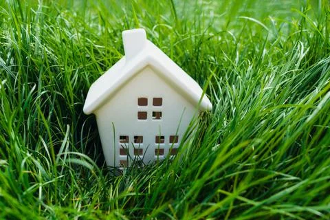Tiny white ceramic house statuette in bright green high grass. Living in nature Stock Photos