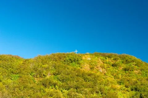 Tiny white cross on a large mountain peak against a clear blue sky. Stock Photos