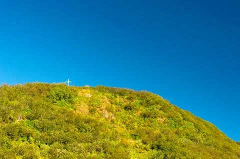 Tiny white cross on a large mountain peak against a clear blue sky. Stock Photos