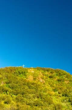 Tiny white cross on a large mountain peak against a clear blue sky. Stock Photos