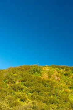Tiny white cross on a large mountain peak against a clear blue sky. Stock Photos