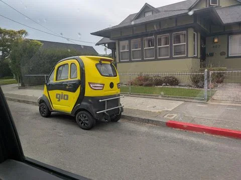 Tiny yellow and black Gio microcar parked 库存照片