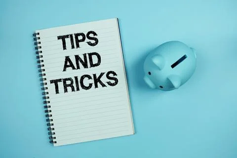 Tips And Tricks text on notebook paper and piggy bank on blue background Stock Photos