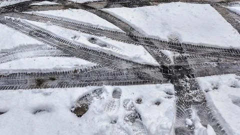 Tire tracks and footprints pressed into fresh snow on a paved surface Stock Photos