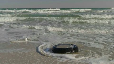 The tire from the wheel is washed by waves on the sandy beach. Stock Footage 80716647