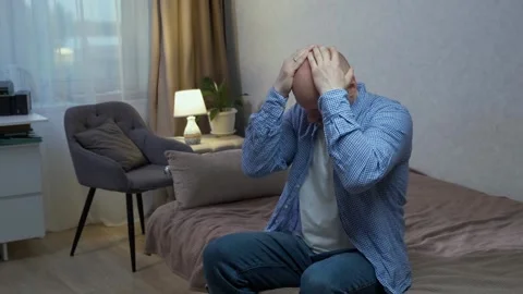 A tired and exhausted bald man suffers from depression sitting on the sofa Stock Footage 242599696