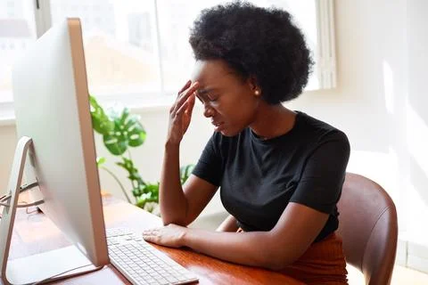 Tired and upset young developer sits with head in hands at desk, Black woman 스톡 사진
