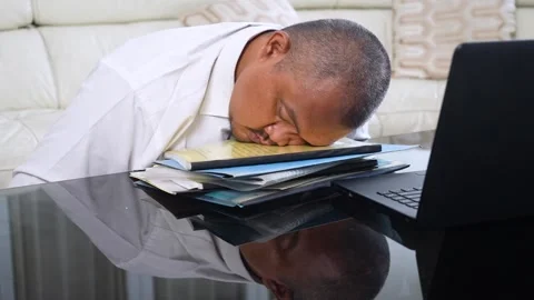 Tired Asian businessman sleeping on a stack of folders next to a laptop at .. Stock Footage 337940452