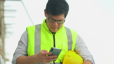 Tired asian foreman take a break and using smartphone outdoors on constructio Stock Footage 146444807