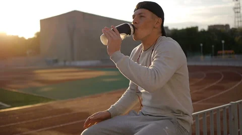 The tired athlete with baseball cap drinks water from the bottle on stadium Stock Footage 64021150